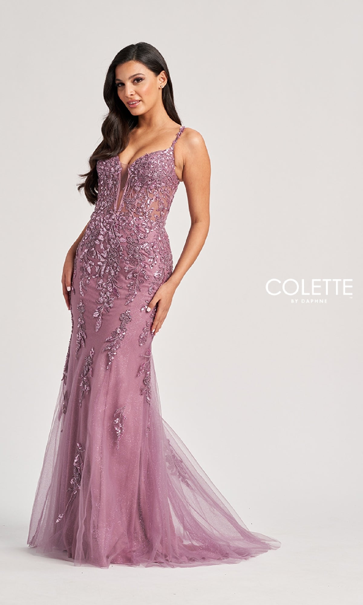 A woman models the Colette CL8210 long prom dress—a fitted, sleeveless lavender lace gown with floral embellishments and a mermaid silhouette—against a plain light background.